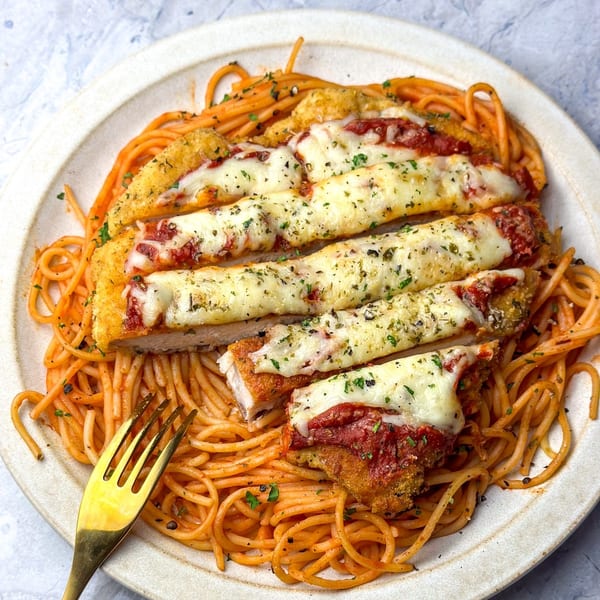 Chicken parmesan with melted cheese and tomato sauce, served over spaghetti with a gold fork.